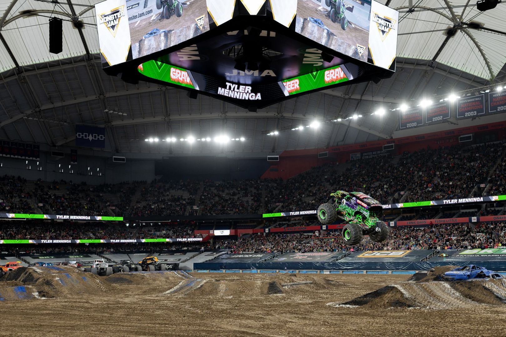 A green monster truck jumps high in the air during a stadium motorsport event.